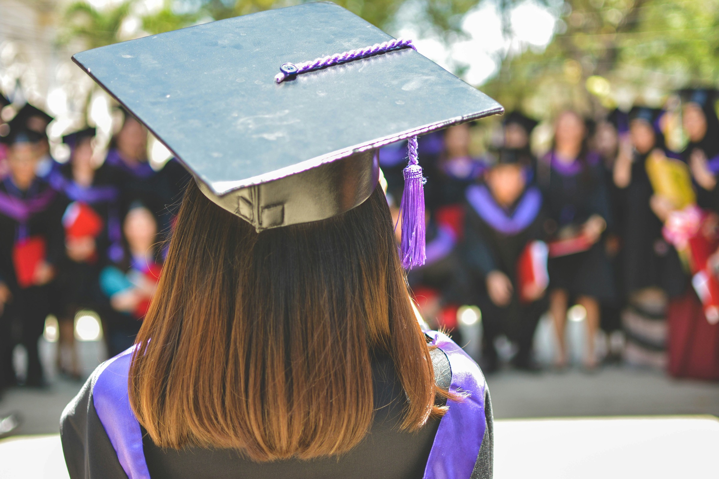 A graduate in cap and gown facing her classmates
